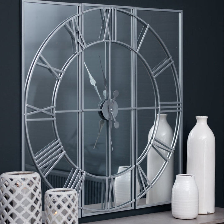 Decorative wall mirror with Roman numeral design on a dark wall with white vases.