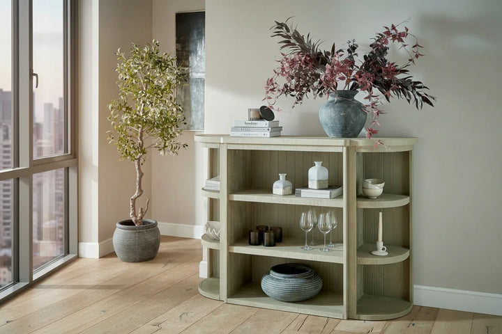 Light wooden shelf with decorative items in a room with large windows.