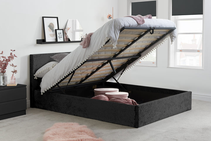 Black upholstered bed with storage drawers in a bedroom setting.