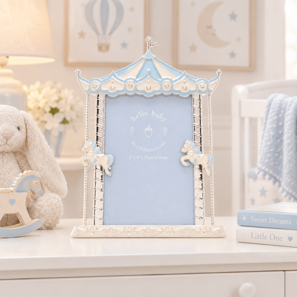 A decorative baby photo frame styled like a carousel, featuring a light blue central panel and pale blue trim with cream-colored carousel details. The frame is displayed on a white dresser alongside a plush bunny toy, books, and a soft crib blanket in a nursery setting.