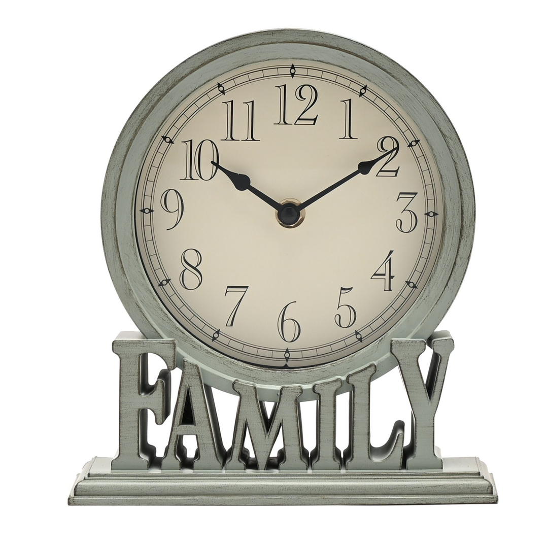 A round wall clock with a distressed sage green frame and base, featuring a cream-colored face and black numerals. The clock is mounted on a matching distressed metal stand with the word 'FAMILY' cut out in large letters, set against a plain white background.